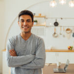 portrait of smart smiling caucasian man standing with arms folded at home posing for photos with copy space